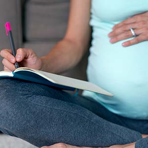 A pregnant woman sits on the couch, taking notes and weighing the pros and cons of a C-section.